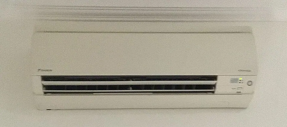 A wall mounted inverter indoor unit in white, the louvre open across its full width and a small control display at the right-hand end.