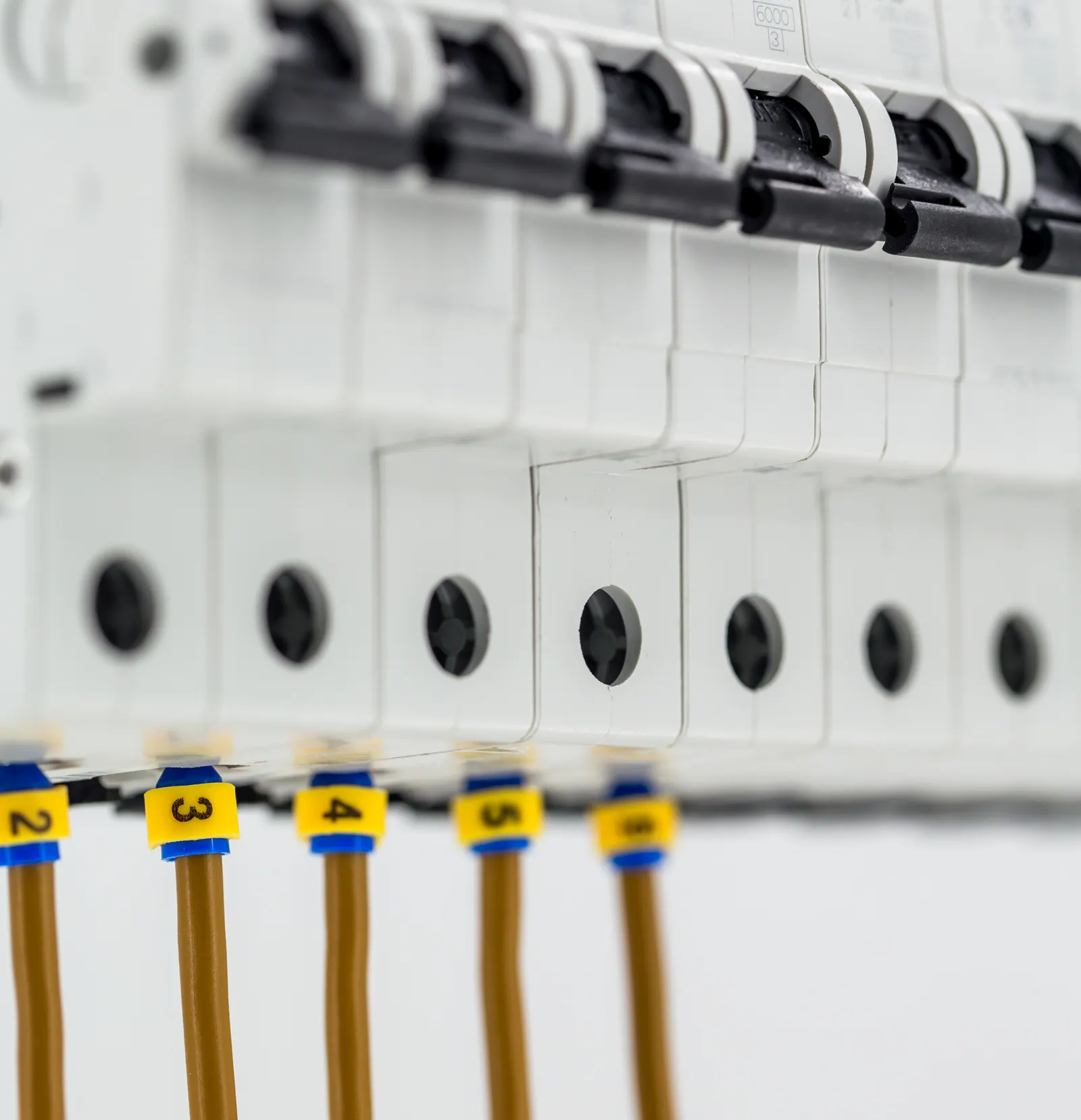 Close up of a row of circuit breakers in a consumer unit, with numbered yellow markers on the cables below.