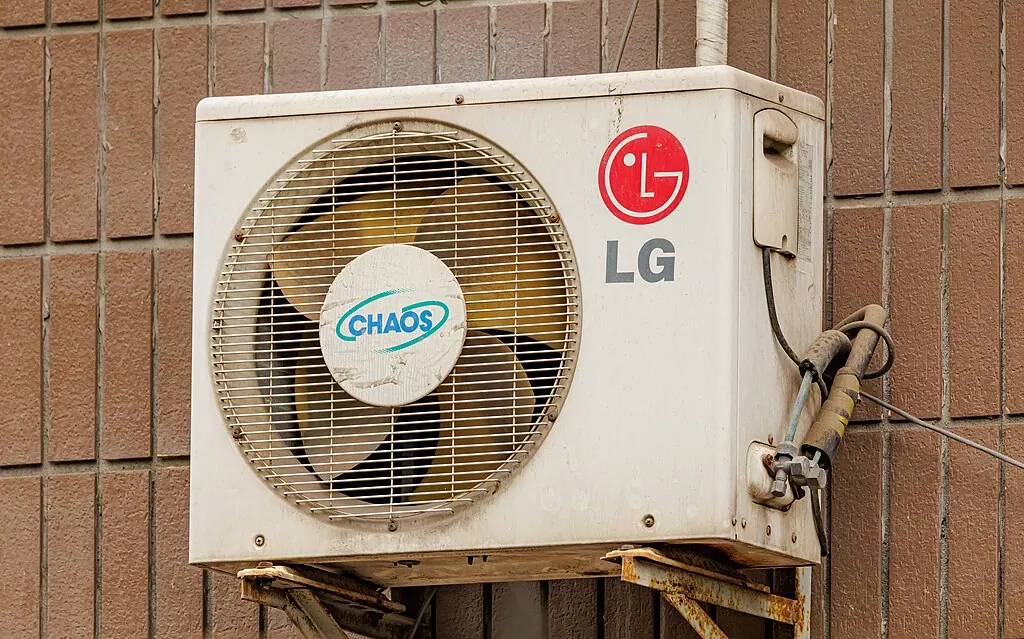 A weathered LG outdoor air conditioning unit on a brick wall, the fan grille discoloured and the bracket rusting.